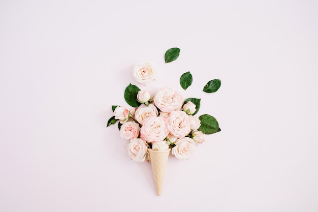 Cône de gaufre avec bouquet de roses bombastiques roses sur fond rose pastel pâle. Mise à plat