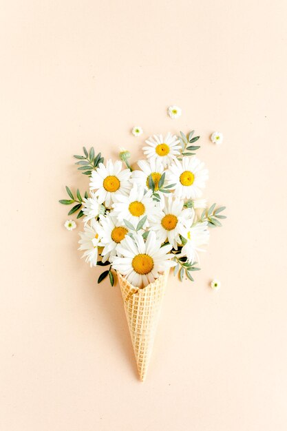 Cône de gaufre avec feuilles de fleurs de camomille sur fond beige plat vue de dessus fond floral