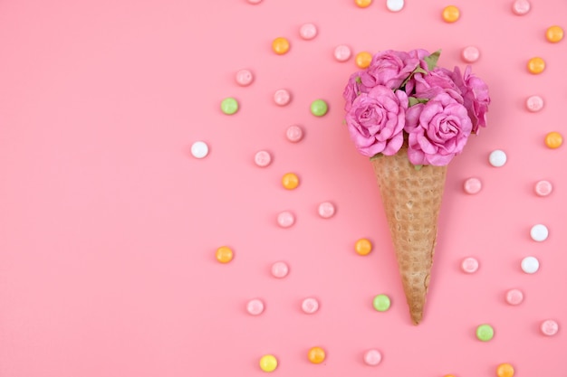 Photo cône de gaufre avec des fleurs et des bonbons colorés sur rose