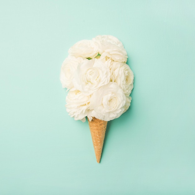 Cône gaufré avec des fleurs de renoncule blanches sur fond bleu pastel