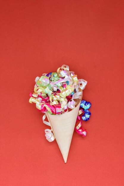 Cone de papier avec des bandes de fête colorées sur fond rouge