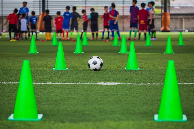 Cône de tactique de ballon de football sur le terrain d'herbe avec pour le fond de formation Formation des enfants au football