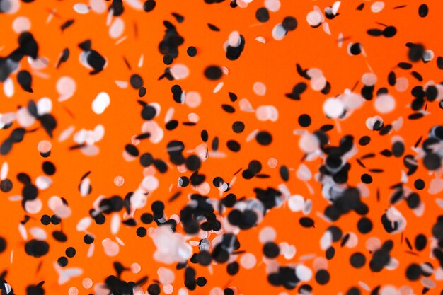 Confettis noirs blancs volant sur la fête d'halloween de fond orange