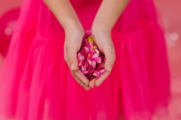 Confettis en papier rose vif et or dans les paumes d'une fille d'anniversaire vêtue d'une robe lors d'une fête