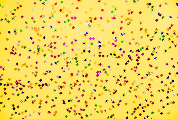 Confettis scintillants colorés en forme d'étoile dispersée sur fond jaune.