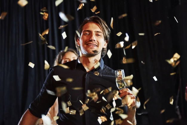 Des confettis sont dans l'air. Groupe d'amis joyeux célébrant le nouvel an à l'intérieur avec des boissons à la main.