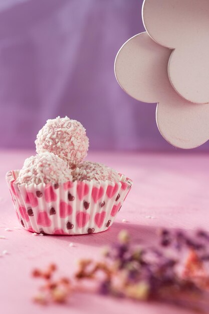 Des conffets blancs saupoudrés de copeaux de noix de coco se trouvent sur un fond rose bonbon en forme de coeur