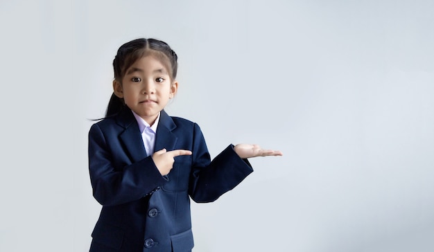 Confiance enfant asiatique en uniforme main ouverte et point à présenter dans l'espace