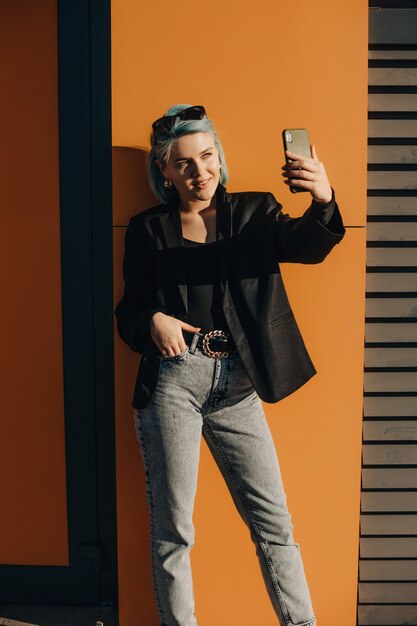 Confiant dame caucasienne aux cheveux bleus faisant un selfie à l'extérieur devant le soleil