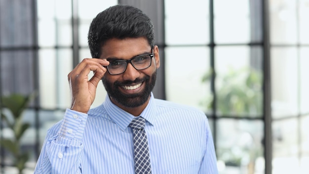 Confiant élégant beau jeune homme debout dans le bureau portant une chemise bleue