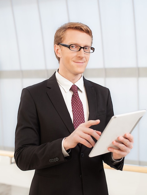 Confiant et intelligent. Jeune homme confiant en tenue de soirée tenant une tablette numérique et regardant la caméra