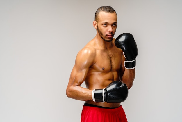 Confiant jeune boxeur africain en gants de boxe debout sur un mur gris clair