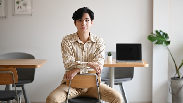 Confiant jeune entrepreneur asiatique assis dans un bureau lumineux et regardant la caméra.