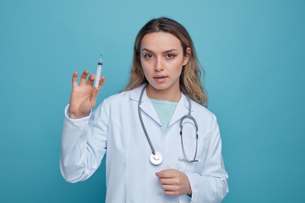 Confiant jeune femme médecin portant une robe médicale et un stéthoscope autour du cou tenant la seringue