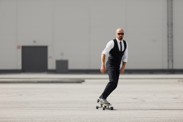 Confiant jeune homme d'affaires à lunettes marchant dans la rue, à l'aide de longboard.