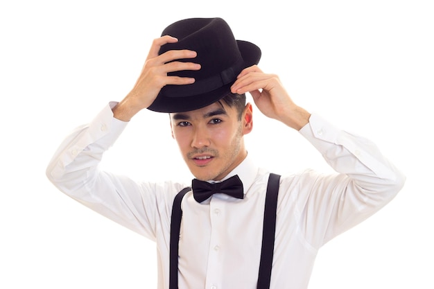 Confiant jeune homme en chemise blanche avec bretelles noeud papillon noir et chapeau en studio