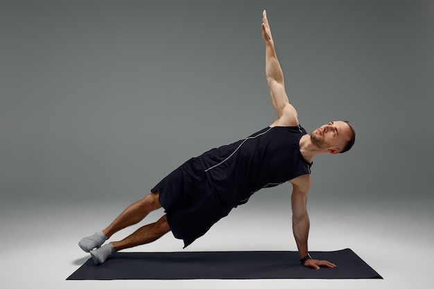 Confiant jeune homme de fitness exerçant sur un tapis de fitness à l'intérieur sur fond de mur gris