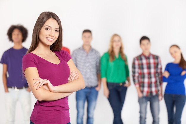 Confiant en sa beauté. Cheerful young woman gardant les bras croisés et souriant tandis que ses amis debout sur fond