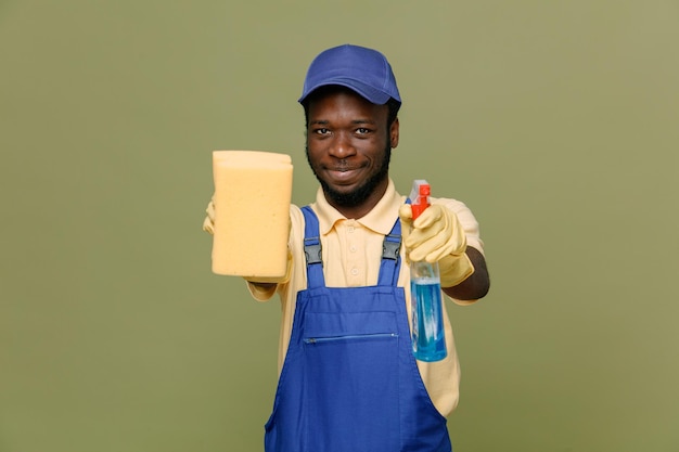 Confiant tenant un agent de nettoyage avec une éponge jeune homme nettoyant afro-américain en uniforme avec des gants isolés sur fond vert