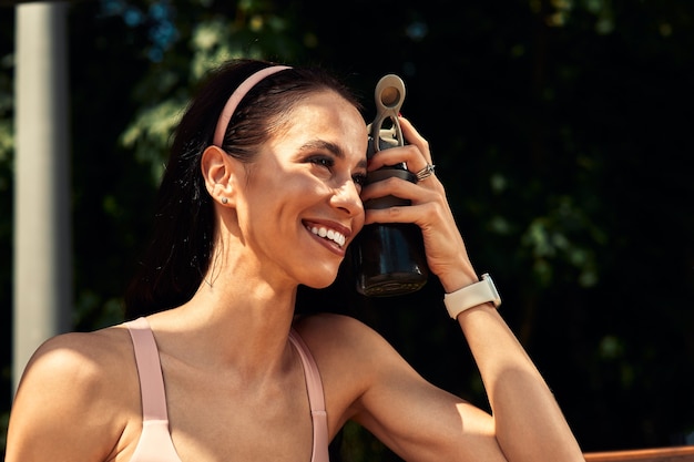 Confiante, belle femme se reposant après l'entraînement en plein air et boit de l'eau d'une bouteille, mène un mode de vie sain.