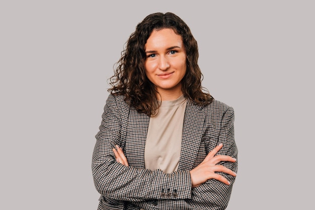 Confiante jeune femme bouclée portant une veste est debout avec les bras croisés