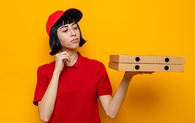 Confiante jeune femme de livraison caucasienne tenant et regardant des boîtes à pizza