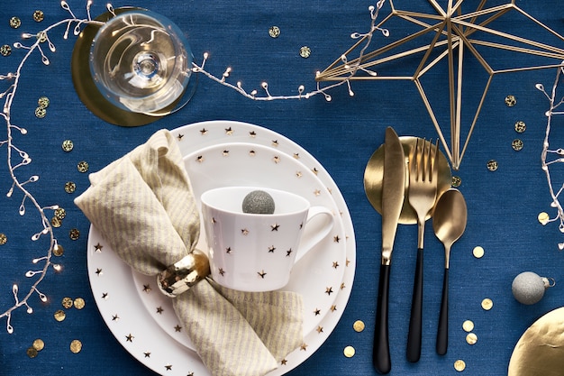 Configuration de table de Noël avec assiette blanche, ustensiles dorés et décor de fil métallique géométrique doré