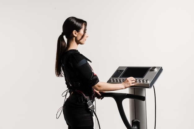 Configurer l'appareil EMS pour l'entraînement sportif d'entraînement en costume de stimulation musculaire électrique sur fond blanc L'entraîneur de fille configure l'appareil EMS avant l'entraînement