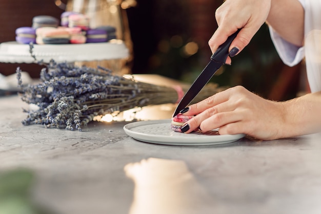 Le confiseur coupe le macaron avec un couteau. Bouchent les mains du chef féminin. Préparation d'un dessert savoureux.