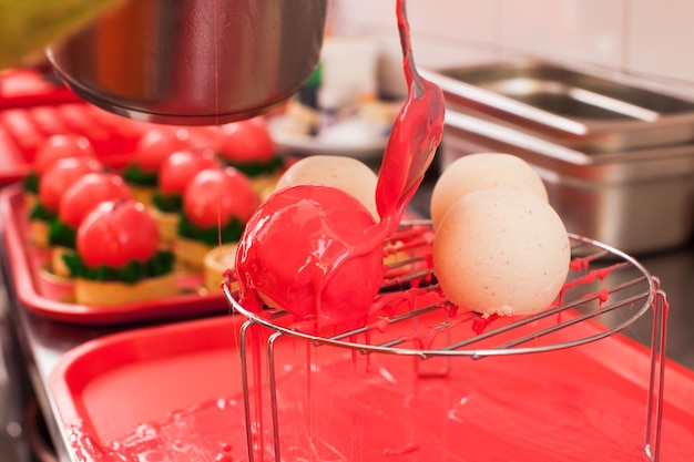 Le confiseur couvre des gâteaux mousse sphériques avec du glaçage rouge Le concept de cuisiner un merveilleux dessert français