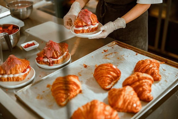 Le confiseur en gants tient une assiette avec un délicieux croissant dans une boulangerie artisanale