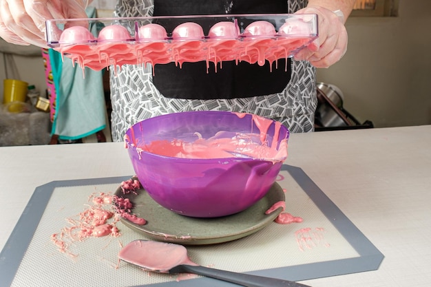 Confiseur versant une casserole en polycarbonate avec une ganache aux fraises dans une capsule (vue de face).