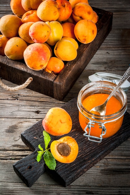 Confiture d'abricot bio maison dans de petits pots, sur une vieille table en bois rustique, avec des abricots et des feuilles de menthe