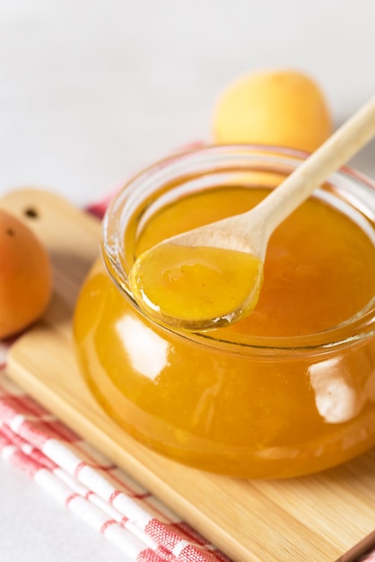 Confiture d'abricot fraîche et savoureuse dans un bocal en verre sur une cuillère en bois de serviette en bois au-dessus de la verticale