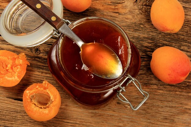 Confiture d'abricots dans un bocal en verre sur une vieille planche de surface en bois