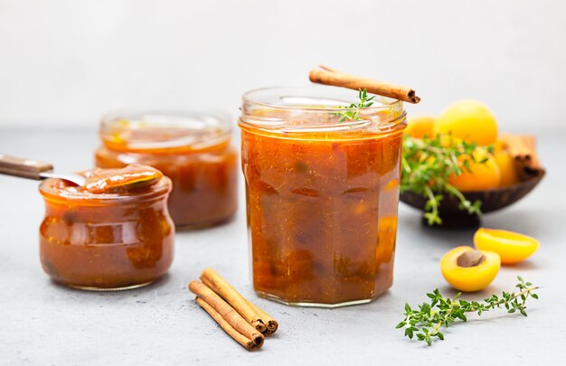 Confiture bio maison dans des bocaux en verre, abricots mûrs, cannelle et thym sur surface grise