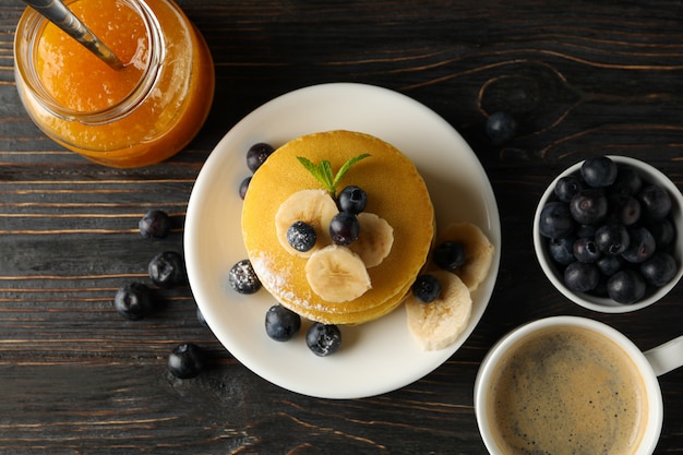 Confiture, café, crêpes aux bleuets et banane sur un espace en bois