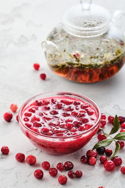 Confiture de canneberges dans un bol en verre et théière sur fond blanc.