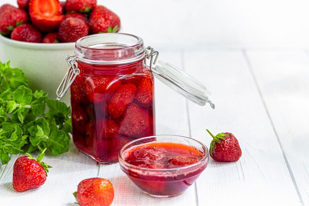 Confiture de fraises dans un bocal en verre à côté de fraises fraîches