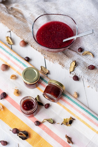 Confiture de framboises sur la table un pot avec de la marmelade rouge sur un décor rustique en tissu de couleur claire à base de feuilles sèches et de noix sainement foodxA