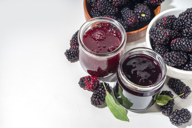 Confiture de mûres maison sucrée dans un petit bocal en verre sur fond blanc, avec espace de copie de baies fraîches