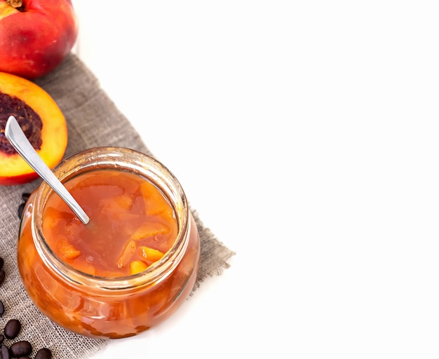 Confiture de nectarine ou de pêche faite maison dans un bocal en verre et une cuillère sur du blanc