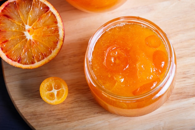 Confiture d'orange et de kumquat dans un bocal en verre avec des fruits frais sur une planche de cuisine en bois