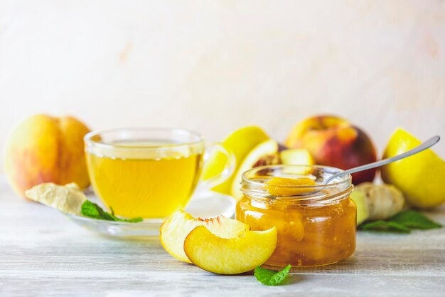 Confiture de pêches fraîches faites maison dans un bocal en verre sur fond de bois Plusieurs baies fraîches citron et menthe