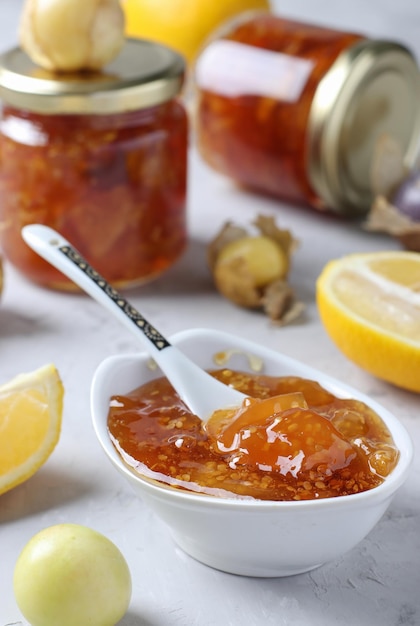 Confiture de physalis transparente faite maison avec du citron dans un bol et des bocaux en verre sur fond gris clair