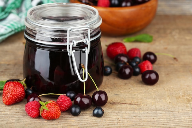 Confiture savoureuse avec des baies dans un bocal en verre sur une table en bois