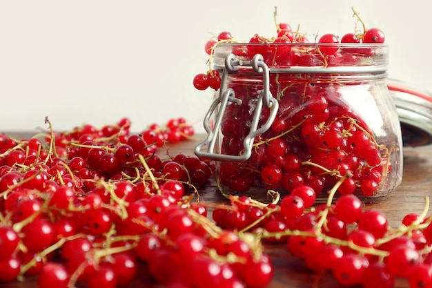 Confiture de vitamines dans un bocal en verre avec des groseilles rouges sur une planche de bois baies autour de l'arrière-plan pour l'espace de gros plan gris pour le texte