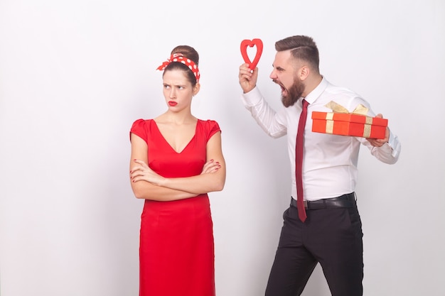 Conflit. La femme ignore l'homme, l'homme d'affaires rugit, tenant un cadeau et un cœur. Intérieur, tourné en studio, isolé sur fond gris