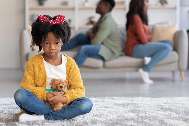 Conflits parentaux triste préadolescente noire assise sur le sol avec un ours en peluche