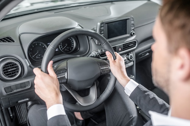 Confort. Homme en costume d'affaires assis dans le siège du conducteur tenant le volant d'une nouvelle voiture à l'écoute des sensations de confort